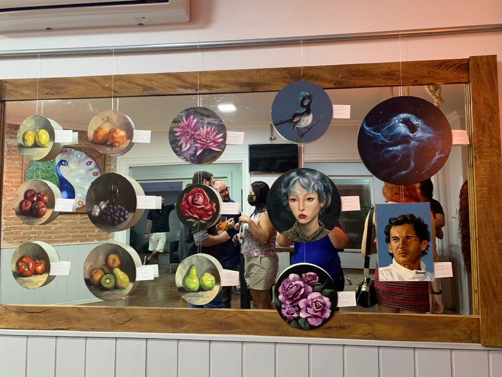 Still-life studies of fruit and flowers on round canvases, with other small works, in a display case at the 2021 launch
